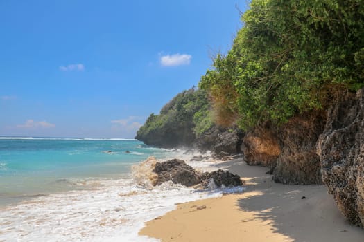 Pantai Gunung Payung beach with fine golden sand, Bali. Turquoise blue water turns into sea foam as the waves break against rocky cliffs of the coast. Sunny day with blue sky. Tourist natural concept.