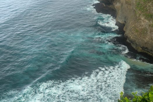 Overview panorama ocean shore, cliff. Sunset. Bali. Overwhelmed scene the flower and green-capped vertical cliff over the Indian ocean. South of Bali island, Pura Luhur Uluwatu Temple. Indonesia.