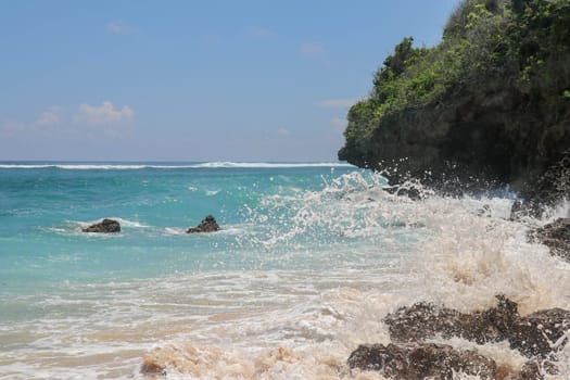Pantai Gunung Payung beach with fine golden sand, Bali. Turquoise blue water turns into sea foam as the waves break against rocky cliffs of the coast. Sunny day with blue sky. Tourist natural concept.