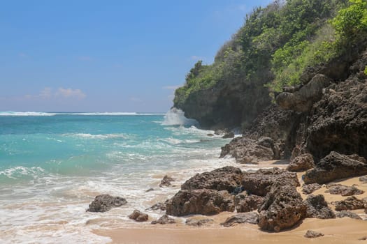 Pantai Gunung Payung beach with fine golden sand, Bali. Turquoise blue water turns into sea foam as the waves break against rocky cliffs of the coast. Sunny day with blue sky. Tourist natural concept.