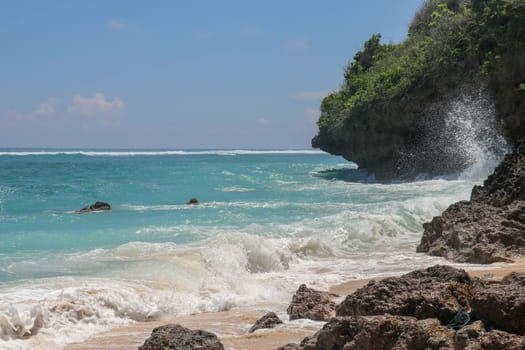 Pantai Gunung Payung beach with fine golden sand, Bali. Turquoise blue water turns into sea foam as the waves break against rocky cliffs of the coast. Sunny day with blue sky. Tourist natural concept.
