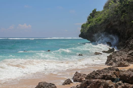 Pantai Gunung Payung beach with fine golden sand, Bali. Turquoise blue water turns into sea foam as the waves break against rocky cliffs of the coast. Sunny day with blue sky. Tourist natural concept.