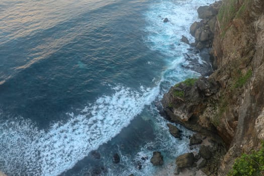 Overview panorama ocean shore, cliff. Sunset. Bali. Overwhelmed scene the flower and green-capped vertical cliff over the Indian ocean. South of Bali island, Pura Luhur Uluwatu Temple. Indonesia.