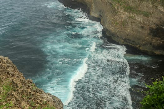 Overview panorama ocean shore, cliff. Sunset. Bali. Overwhelmed scene the flower and green-capped vertical cliff over the Indian ocean. South of Bali island, Pura Luhur Uluwatu Temple. Indonesia.