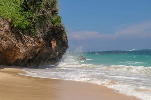 Pantai Gunung Payung beach with fine golden sand, Bali. Turquoise blue water turns into sea foam as the waves break against rocky cliffs of the coast. Sunny day with blue sky. Tourist natural concept.