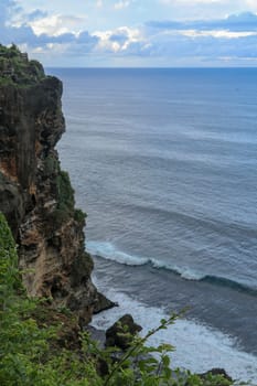 Overview panorama ocean shore, cliff. Sunset. Bali. Overwhelmed scene the flower and green-capped vertical cliff over the Indian ocean. South of Bali island, Pura Luhur Uluwatu Temple. Indonesia.