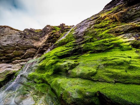 Beautiful waterfall over mossy stones in the Cove of Tintagel in Cornwall