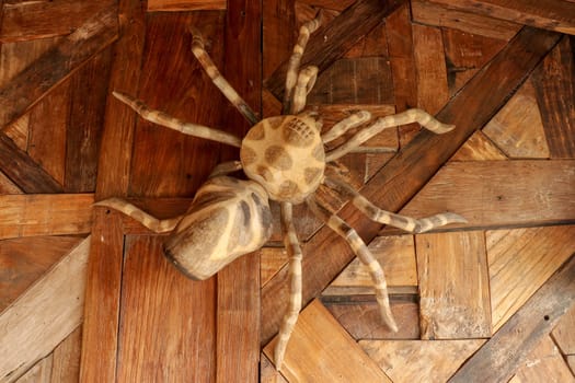 Large tarantula on the wall of rough planed planks. Statue Huge spider made of wood. Brown toy spider on the wooden floor. Selective focus.