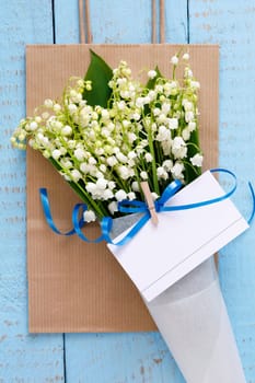 Lily of the valley flowers in a paper bag on blue background. Flat lay, top view, copy space