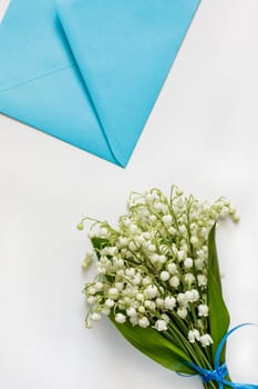 Bouquet of lilies of the valley and a blue envelope on a white table