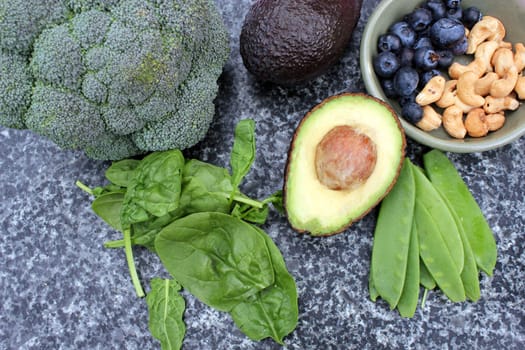 Vegan vegetarian plant based diet gluten free selection of cashew nuts, blueberries, spinach, mange tois peas avocado and broccoli on marble and board background