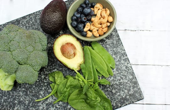 Vegan vegetarian plant based diet gluten free selection of cashew nuts, blueberries, spinach, mange tois peas avocado and broccoli on marble and board background