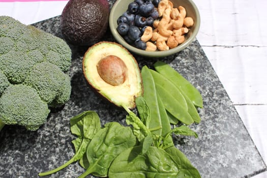 Vegan vegetarian plant based diet gluten free selection of cashew nuts, blueberries, spinach, mange tois peas avocado and broccoli on marble and board background