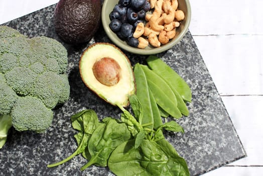Vegan vegetarian plant based diet gluten free selection of cashew nuts, blueberries, spinach, mange tois peas avocado and broccoli on marble and board background