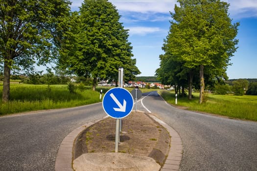 Country road with blue traffic sign and trees in summer in Germany