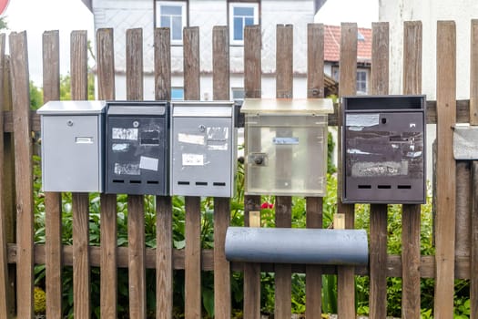 Five dirty and weathered Mail Boxes hanging on a wooden Fence