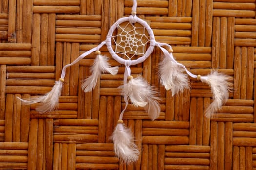 Dream catcher, decorated with white feathers and wooden beads, on a wooden surface. Dream catcher with wooden circle. Knitted Native American amulet with the symbol of Yin Yang on a wodden background.