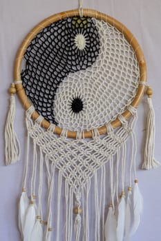 Dream catcher, decorated with white feathers and wooden beads, on a wooden surface. Dream catcher with wooden circle. Knitted Native American amulet with the symbol of Yin Yang on a white background.