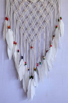 Handmade pink dream catcher with white doily on background of rocks and lake. Tribal elements, feathers, lace, crochet snowflake.