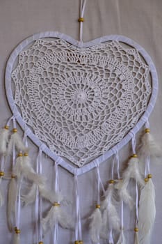 Dream catcher shaped heart with beige peacock feathers in the interior.