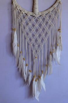 Handmade pink dream catcher with white doily on background of rocks and lake. Tribal elements, feathers, lace, crochet snowflake.