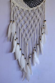 Handmade pink dream catcher with white doily on background of rocks and lake. Tribal elements, feathers, lace, crochet snowflake.