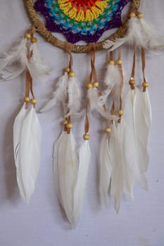 Handmade pink dream catcher with white doily on background of rocks and lake. Tribal elements, feathers, lace, crochet snowflake.
