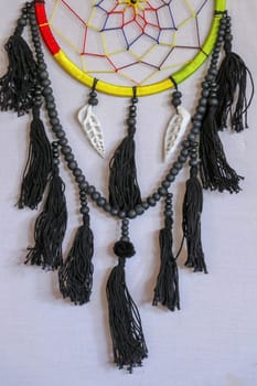 Handmade pink dream catcher with white doily on background of rocks and lake. Tribal elements, feathers, lace, crochet snowflake.