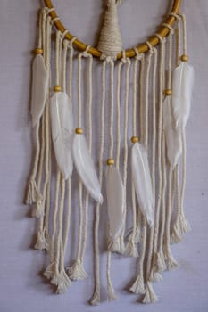 Handmade pink dream catcher with white doily on background of rocks and lake. Tribal elements, feathers, lace, crochet snowflake.