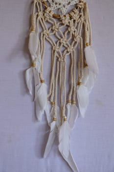 Handmade pink dream catcher with white doily on background of rocks and lake. Tribal elements, feathers, lace, crochet snowflake.