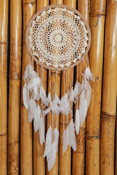 Dream catcher, decorated with white feathers and wooden beads, on a wooden surface. Dream catcher with wooden circle. Knitted Native American amulet with the symbol of Yin Yang on a wodden background.