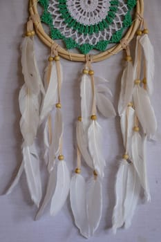 Handmade pink dream catcher with white doily on background of rocks and lake. Tribal elements, feathers, lace, crochet snowflake.