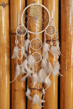 Dream catcher, decorated with white feathers and wooden beads, on a wooden surface. Dream catcher with wooden circle. Knitted Native American amulet with the symbol of Yin Yang on a wodden background.