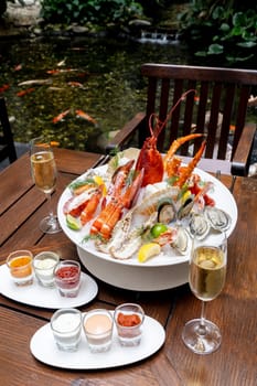 Bowl of gourmet fresh seafood on ice with savory sauce serve with white wine glass on vintage wooden table. Restaurant gastronomy food and drink consumerism concept.