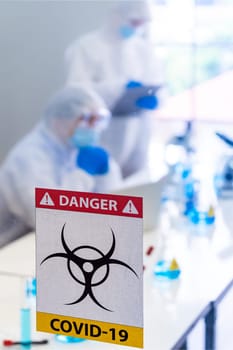Caution danger Signage of COVID-19 coronavirus in front of Laboratory room with background of Scientists working and researching vaccine for ncov-19 virus for world pandemic situation.