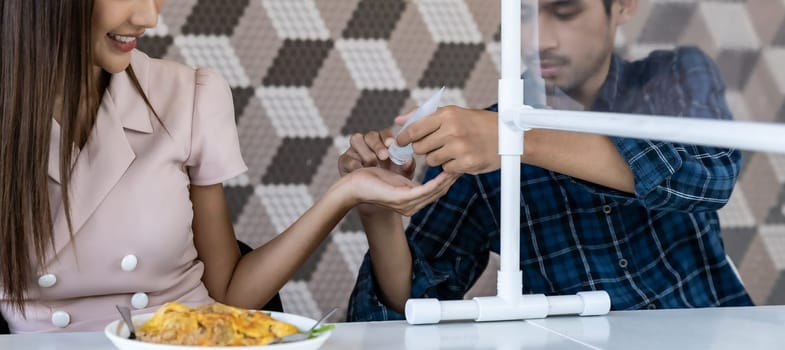 Panoramic asian man put alcohol gel hand sanitizer to his partner before eating at new normal social distance restaurant with table partition. Restaurant new normal lifestyle. Web banner crop.