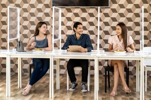 Asian group of friend eating out together at new normal social distance restaurant with table shiled partition reduce infection of coronavirus covid-19 pandemic. Restaurant new normal lifestyle.
