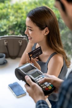 Asian woman customer hold contactless credit card for making online payment after eating out in new normal social distance restaurant. Online contactless and technology concept.
