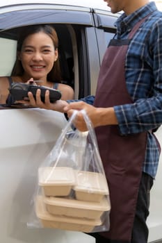Asian woman customer make mobile payment contactless technology on drive thru food service restaurant while picking up. Drive through is new normal more popular after coronavirus covid-19 pandemic.