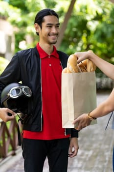 Asian delivery man pick up bakery grocery bag from bakery shop to deliver to customer who make online order. Online food delivery service concept in new normal after coronavirus pandemic.
