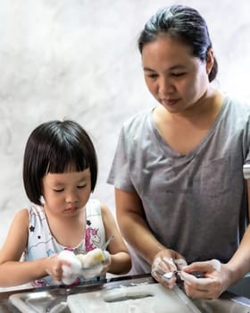 Asian girl washing dish and tableware with her mom, housework for child make executive function for kid. Houseworking for kid lifstyle and family concept.