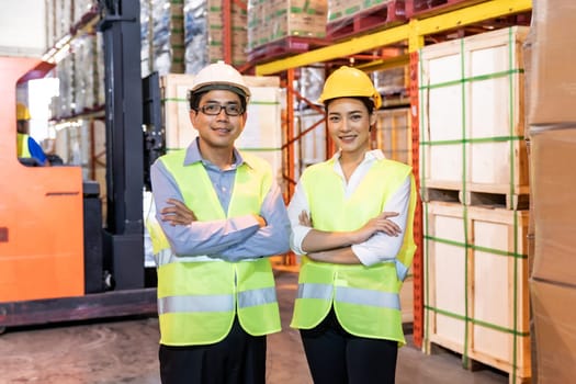 Portrait of Asian warehouse manager and worker arm crossed with warehouse worker operate forklift to check inventory in background. Reopening business warehouse technology and logistic concept.