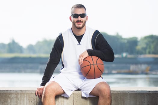 Front view portrait of cool sitting streetball or basketball player outdoors.
