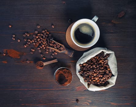 Photo of fresh tasty coffee on vintage wood table background. Coffee cup, coffee beans in canvas bag and ground powder. Top view. Flat lay.