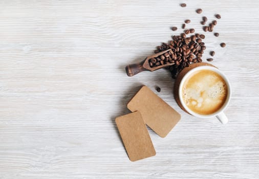 Coffee cup, roasted coffee beans and blank kraft paper business cards on light wood table background. Top view with copy space for your text. Flat lay.