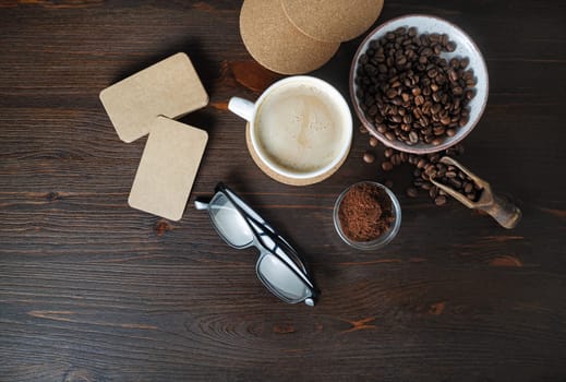 Coffee cup, kraft business cards, roasted coffee beans, glasses and coffee ground on wood table background. Flat lay.