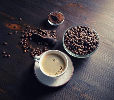 Warm coffee cup, coffee beans and ground powder on brown wooden background.