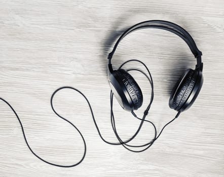 Photo of black dj stereo headphones on light wooden background. Flat lay.