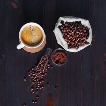 Brewing coffee still life. Coffee cup, coffee beans in canvas bag and ground powder on wood kitchen table background. Top view. Flat lay.