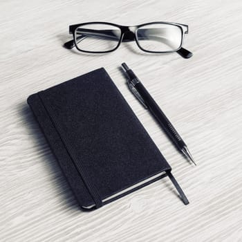 Blank black notepad, glasses and pencil on light wooden background.